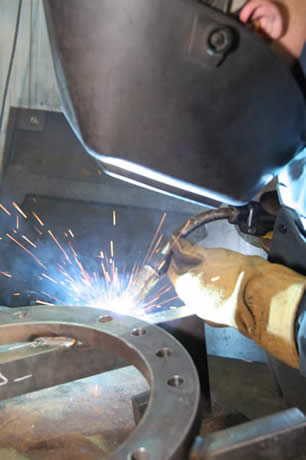 Image of a welder leaning over welding with a MIG gun.
