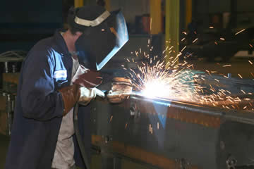 Image of a welder looking closely at an arc with MIG gun in hand