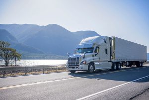 White tractor trailer on road next to lake and mountains